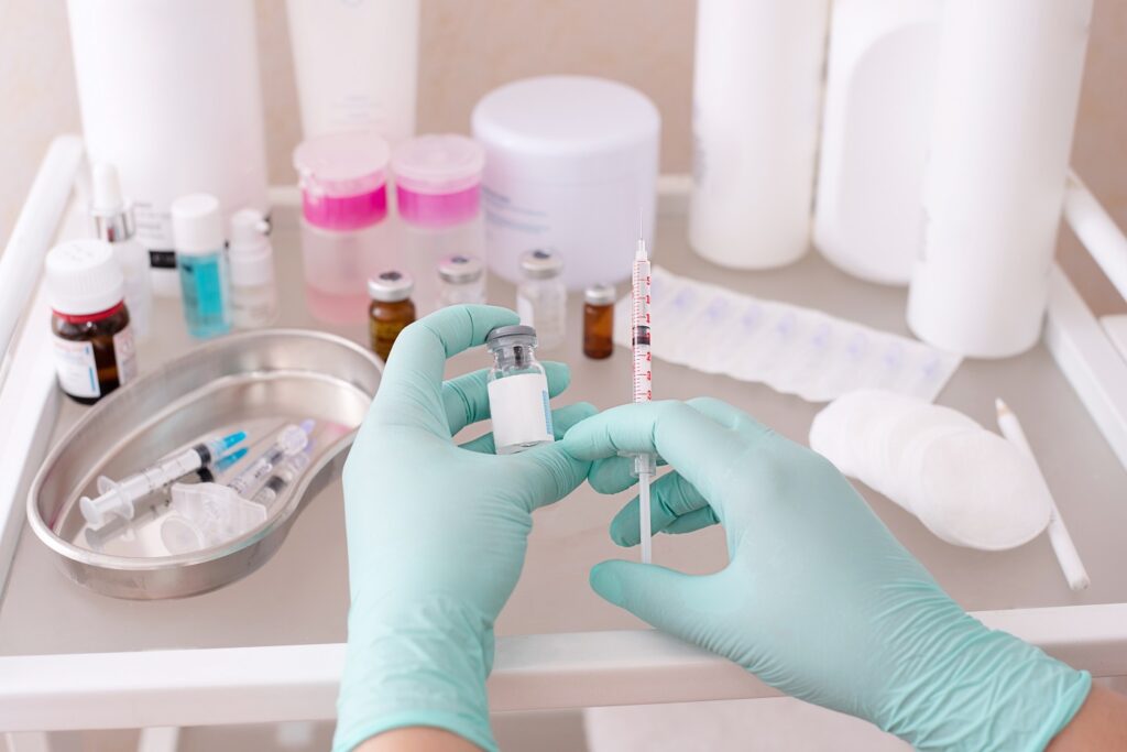 Gloved hands holding a syringe for injection and a bottle of botulinum toxin on the table with rejuvenation products in the beauty parlor, close up.